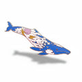Decorative whale-shaped object on a textured surface with small plants and flowers.