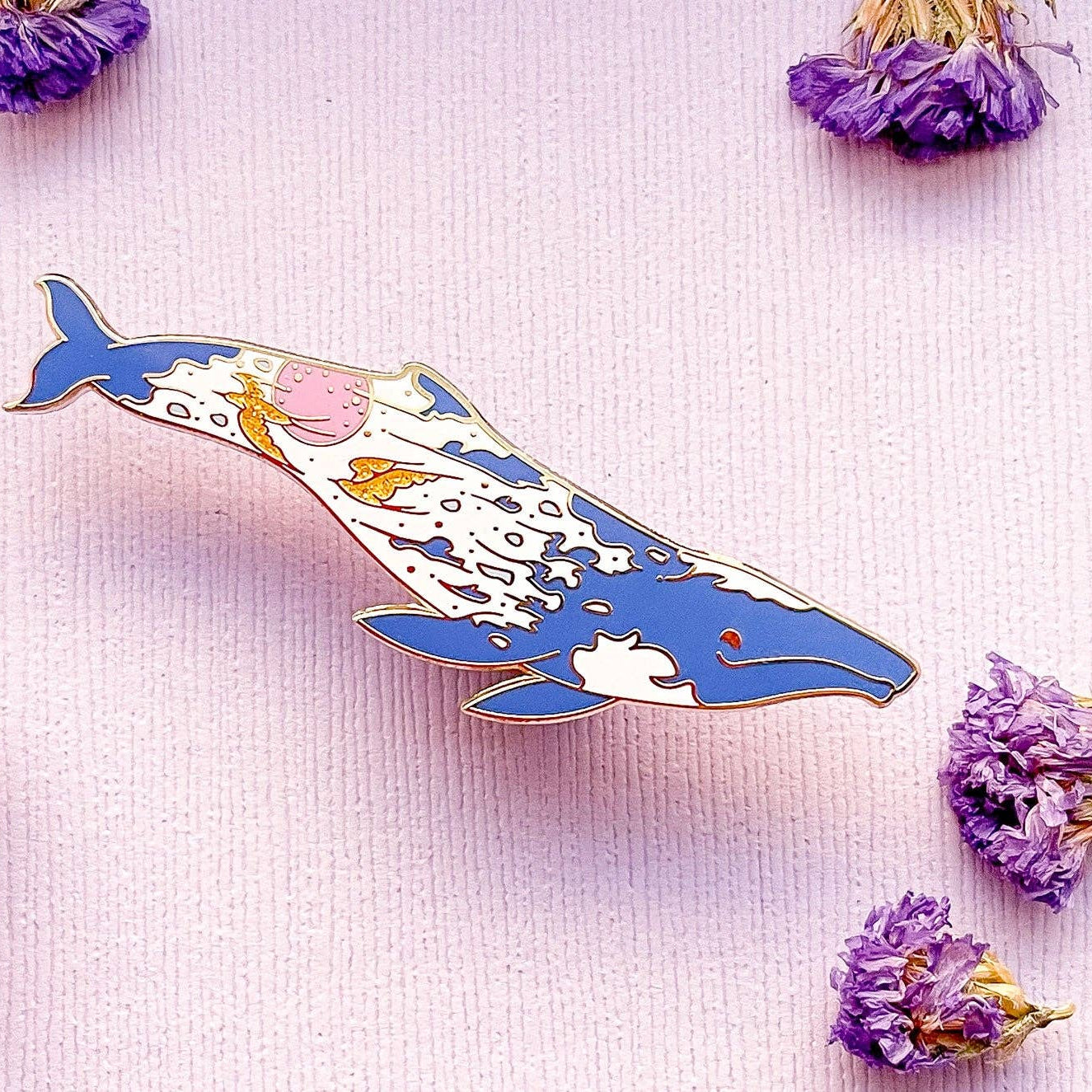 Decorative whale pin on a light pink background with dried flowers