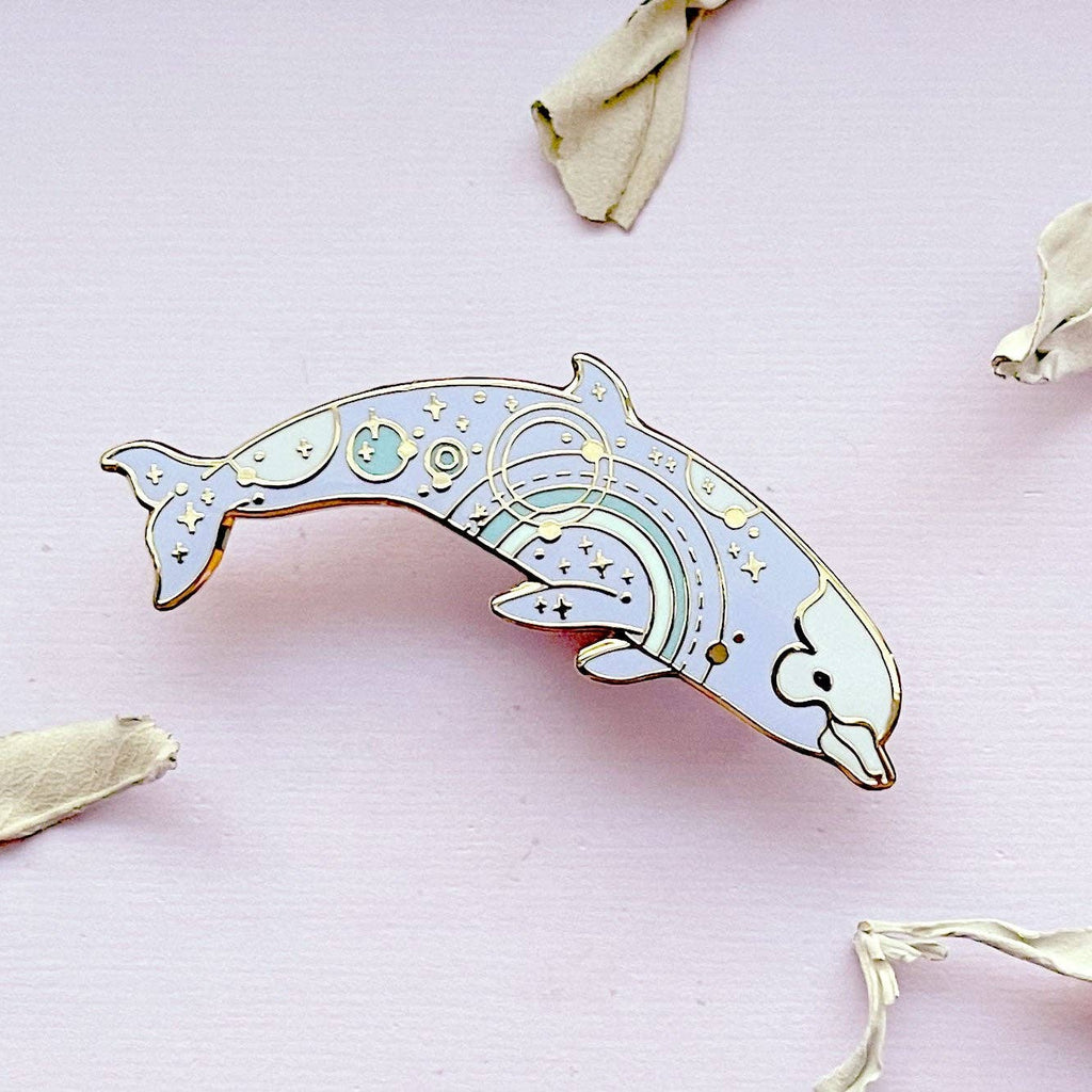 Decorative dolphin pin on a pink background with dried leaves