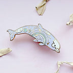 Decorative dolphin pin on a pink background with dried leaves