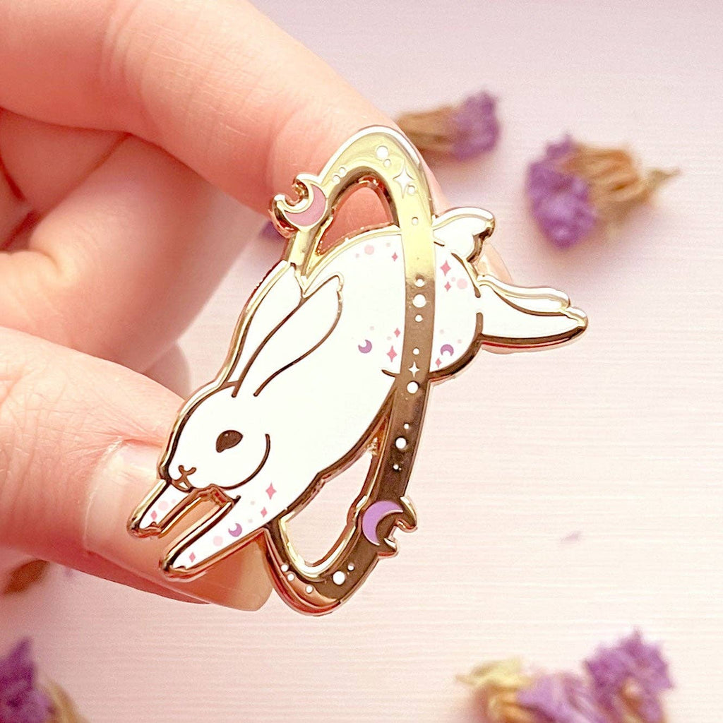 Hand holding a gold rabbit-shaped object with a pink background