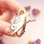 Hand holding a gold rabbit-shaped object with a pink background