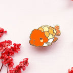Colorful Ranchu Goldfish enamel pin on a background with red flowers.