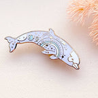Decorative dolphin-shaped pin on a light background with decorative elements