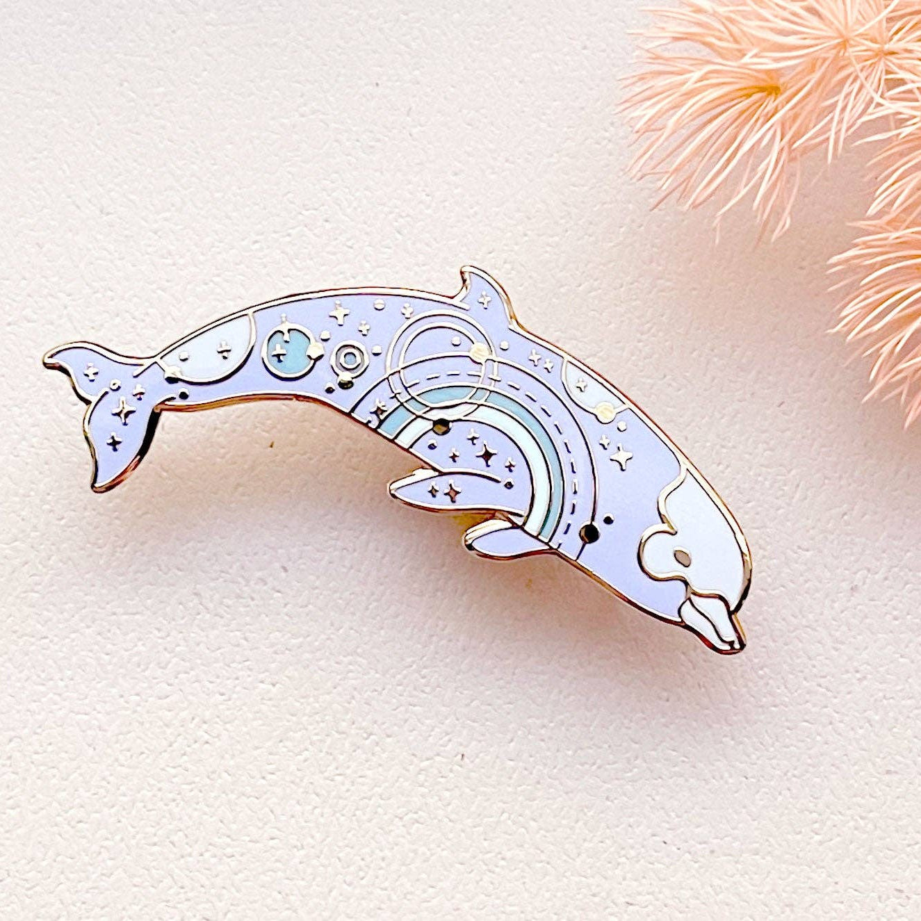 Decorative dolphin-shaped pin on a light background with decorative elements