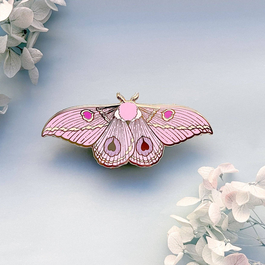 Pink butterfly-shaped moth pin on a light blue background with white flowers.