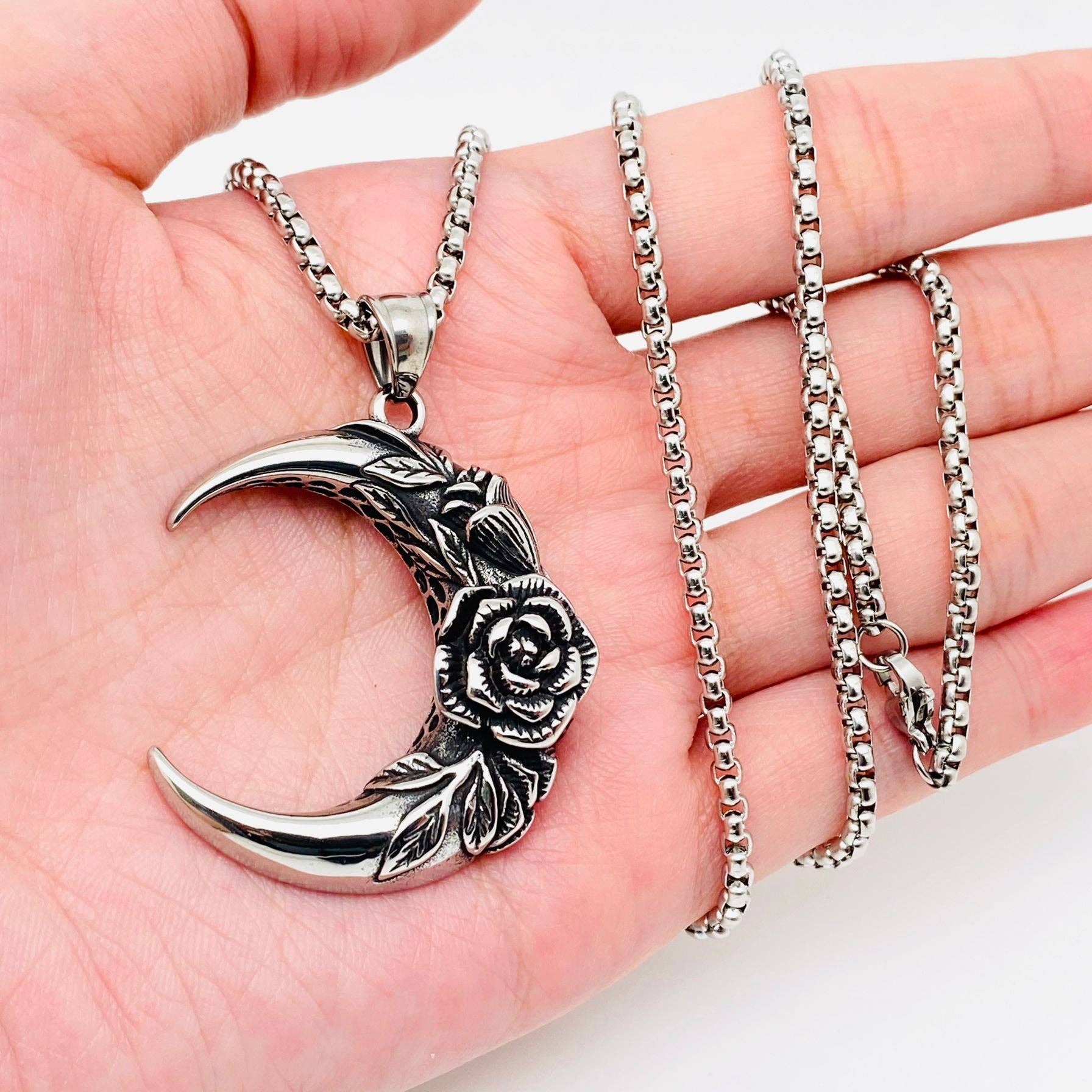 Silver crescent moon and rose pendant on a chain held in a hand.
