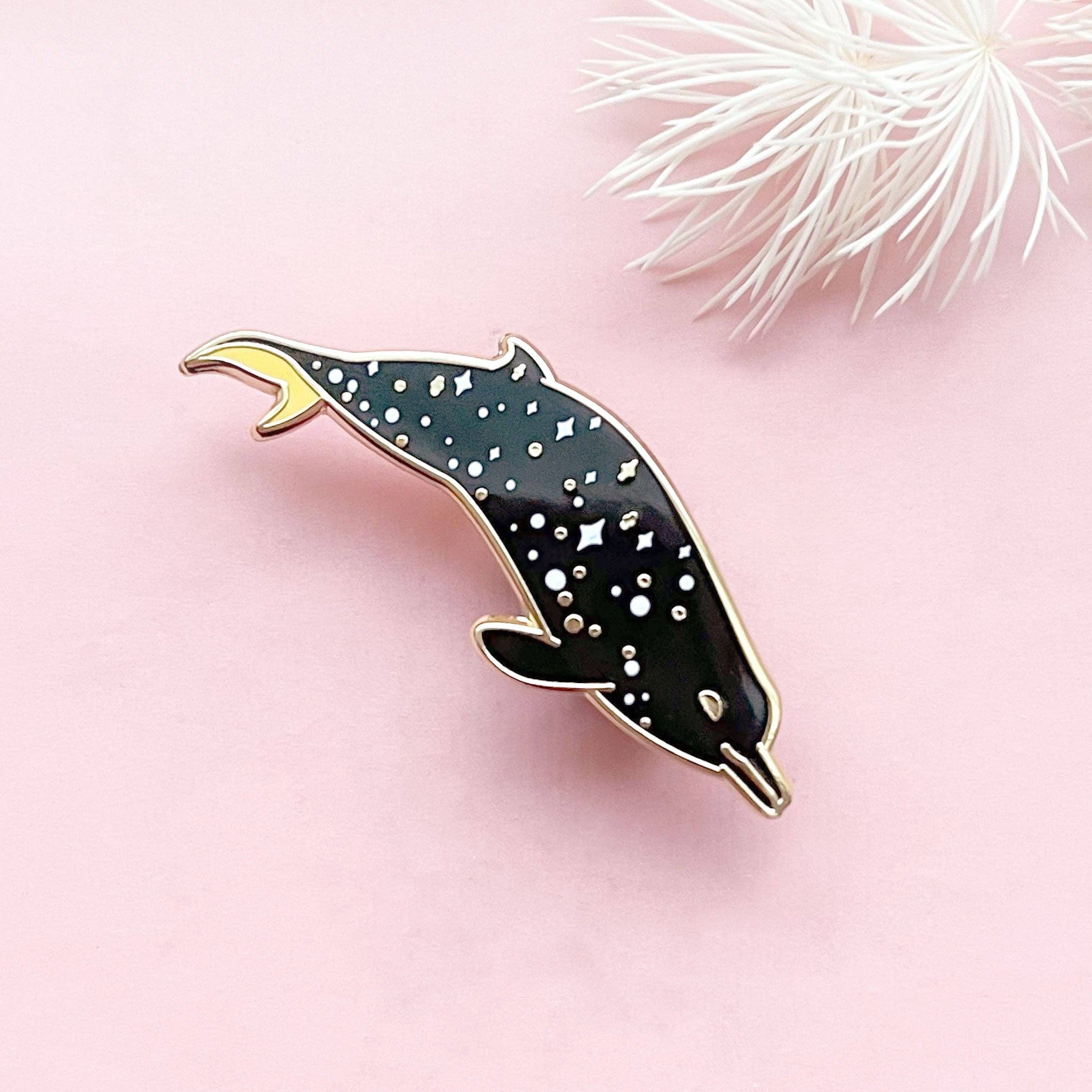 Dolphin-shaped pin on a pink background with decorative elements