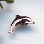 Dolphin-shaped pin on a light blue background with leaves