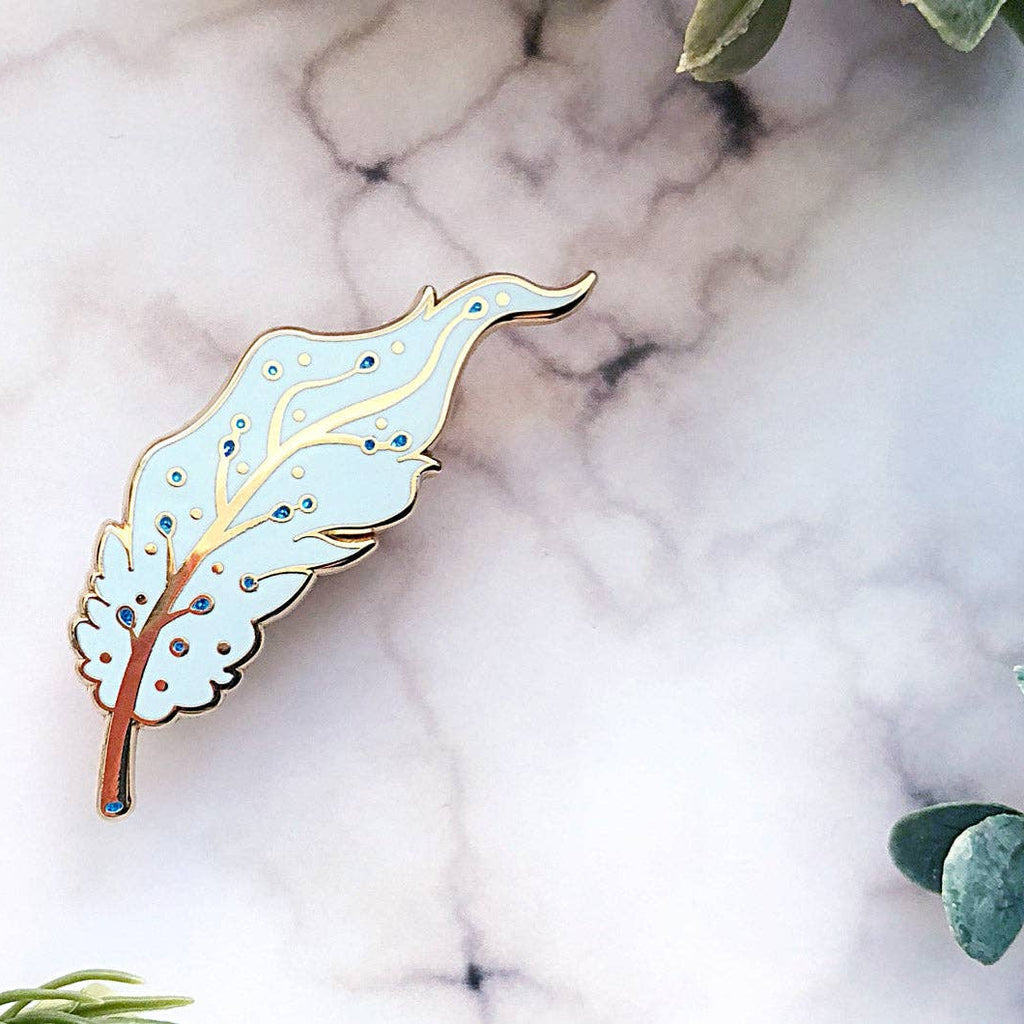 Decorative Pegasus pin on a marble surface with green leaves.
