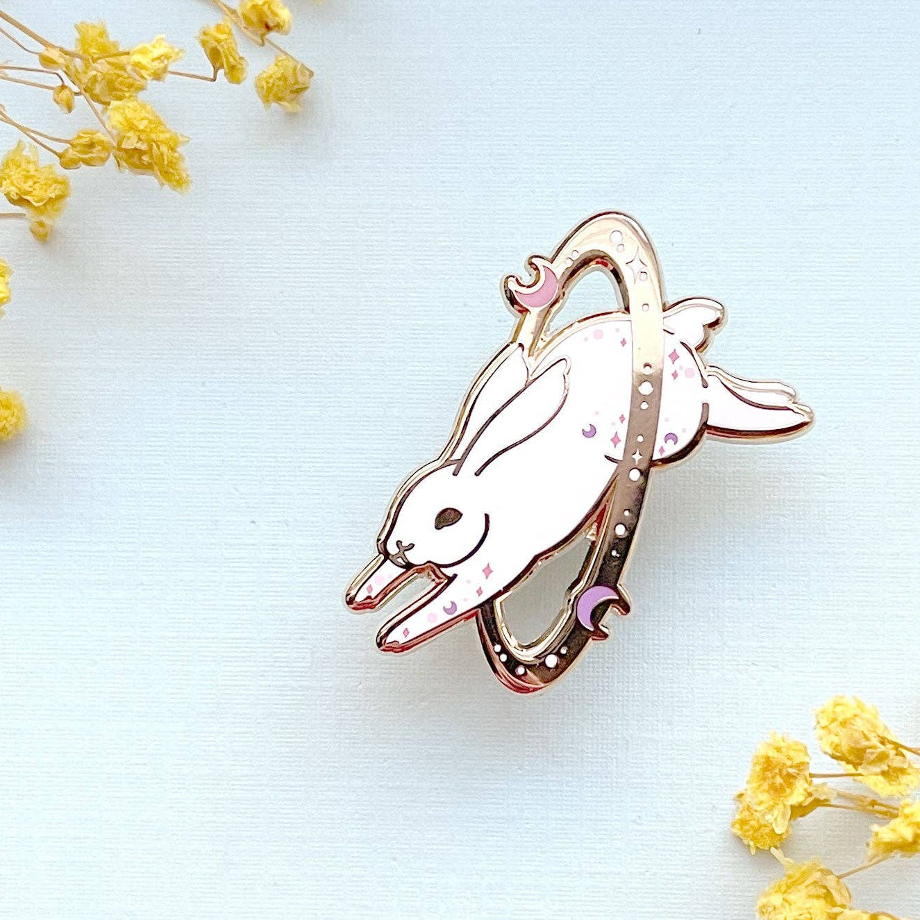 gold-plated cosmic white rabbit pin on a light blue background with yellow flowers