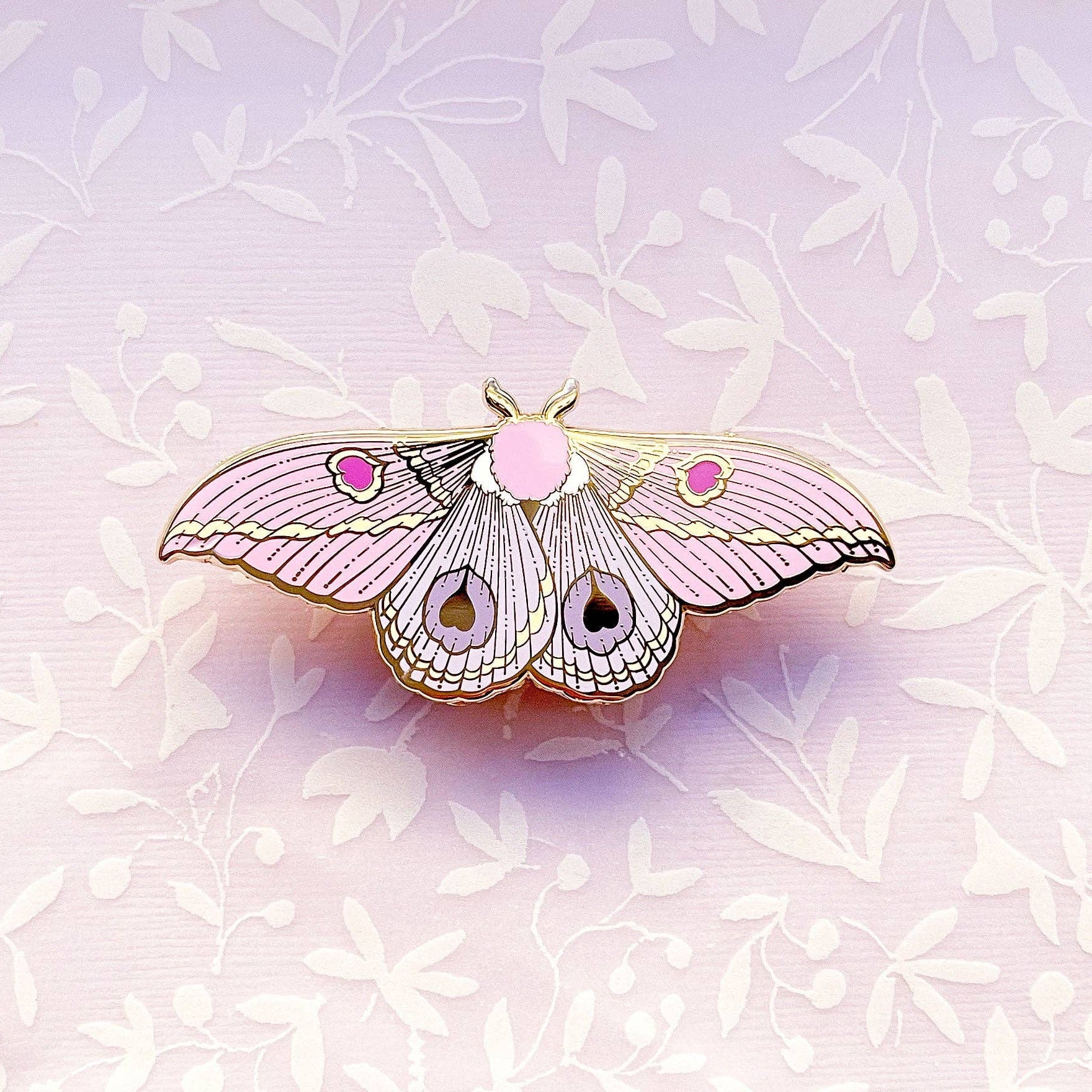 Pink butterfly-shaped moth pin on a light purple floral background