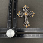 Decorative cross with gold accents on a gray surface next to a ruler for scale.