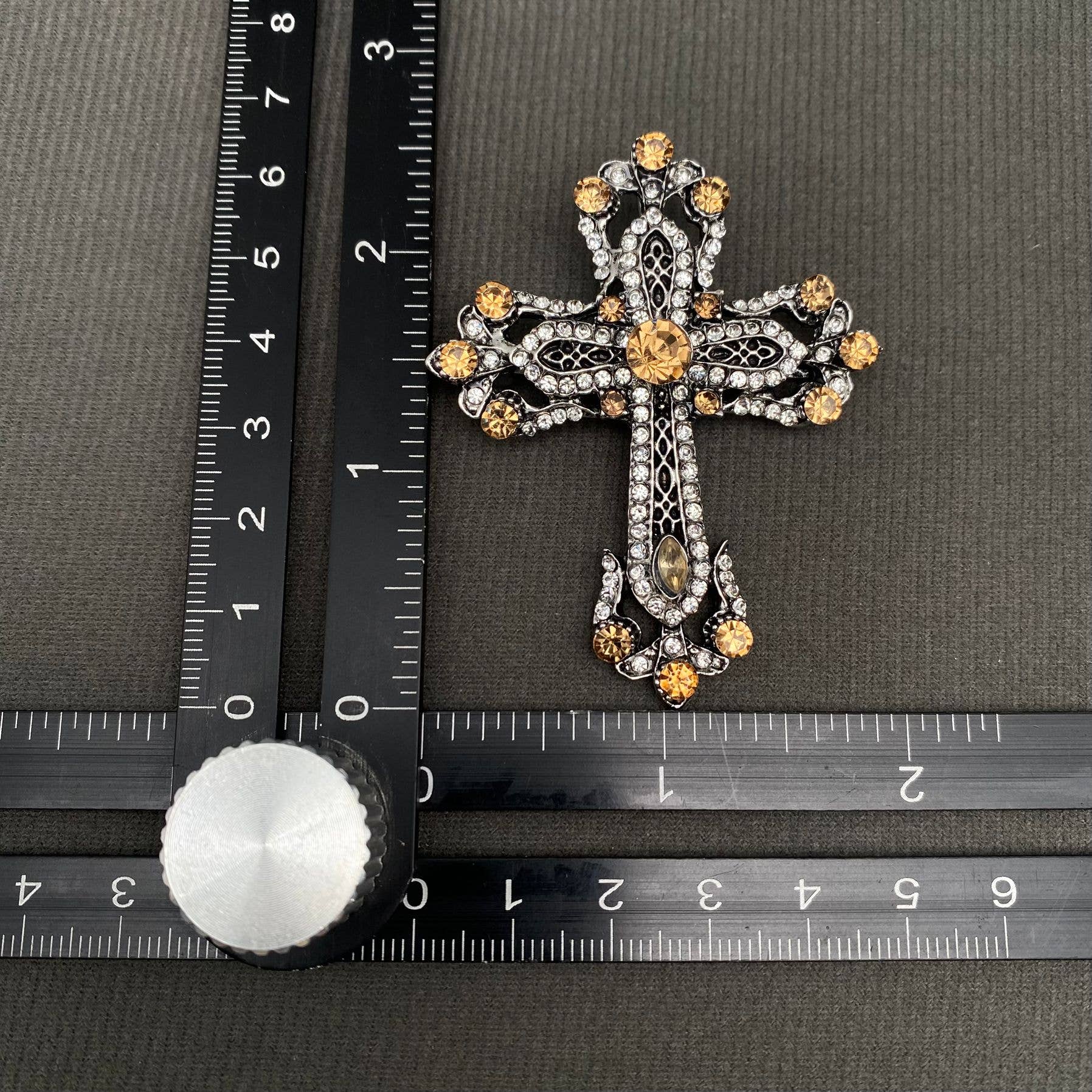Decorative cross with gold accents on a gray surface next to a ruler for scale.