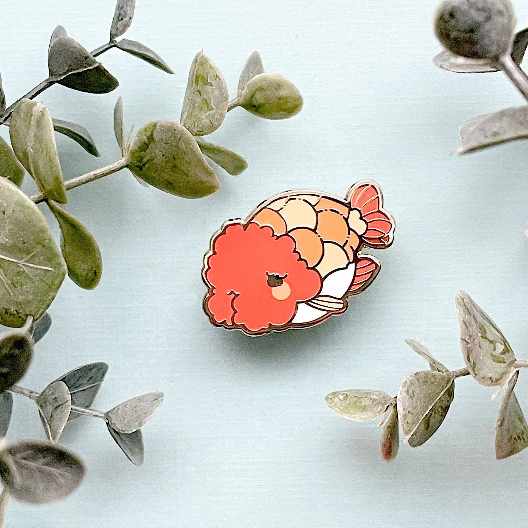 Colorful Ranchu Goldfish pin on a light blue background with green leaves