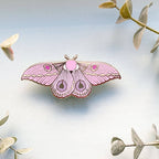 Pink moth-shaped lapel pin on a light background with leaves