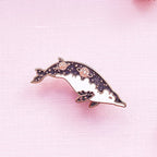 Dolphin-shaped brooch with pink accents on a pink background