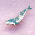 Decorative whale-shaped pin on a pink floral background