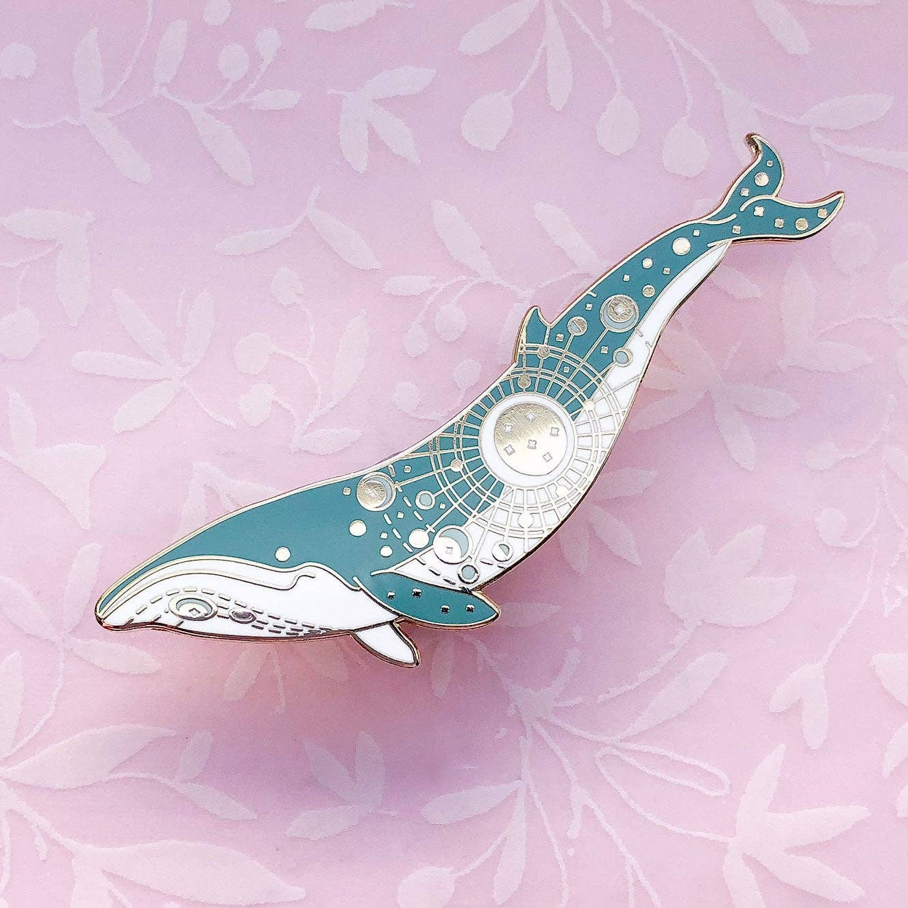 Decorative whale-shaped pin on a pink floral background