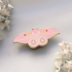 Pink butterfly-shaped moth pin on a light gray background with white flowers.