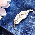Decorative Pegasus feather pin on a denim fabric with pink flowers in the background