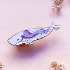 Decorative whale-shaped object with a purple design on a soft pink background