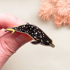 Dolphin-shaped pin held by a hand with a soft, blurred background