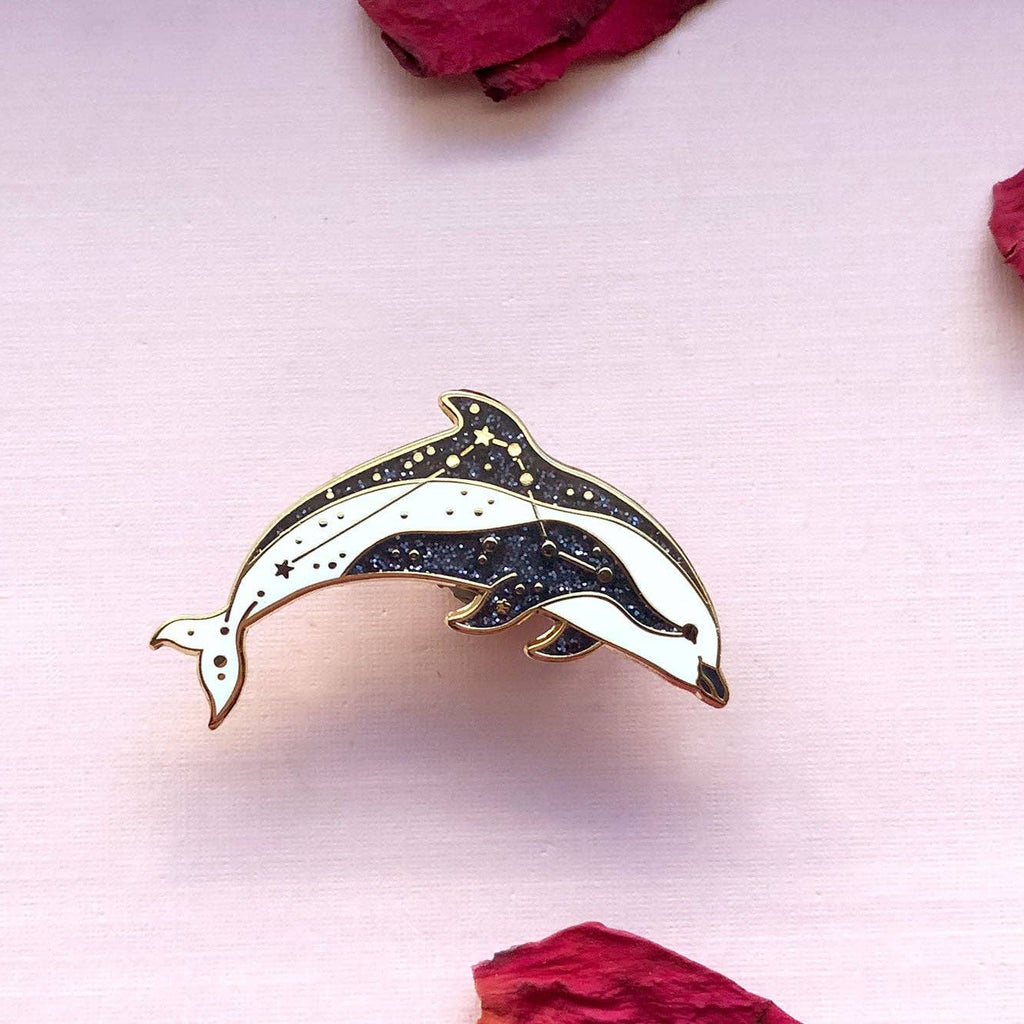 Dolphin-shaped pin on a light pink background with dried roses