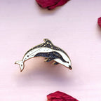 Dolphin-shaped pin on a light pink background with dried roses