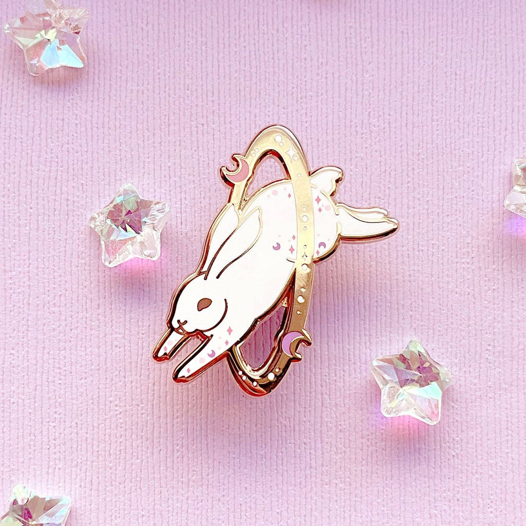 Enamel pin of a rabbit with rose gold border on a pink background with crystals