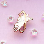 Enamel pin of a rabbit with rose gold border on a pink background with crystals