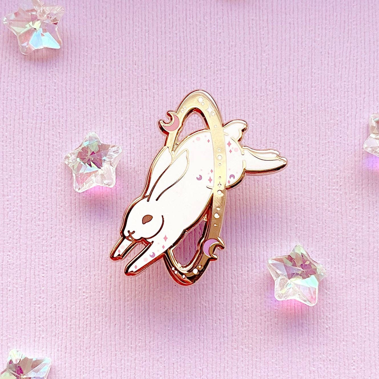 Enamel pin of a rabbit with rose gold border on a pink background with crystals