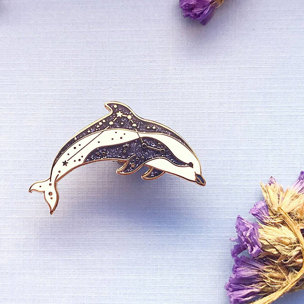 Dolphin-shaped brooch on a light blue background with dried flowers.