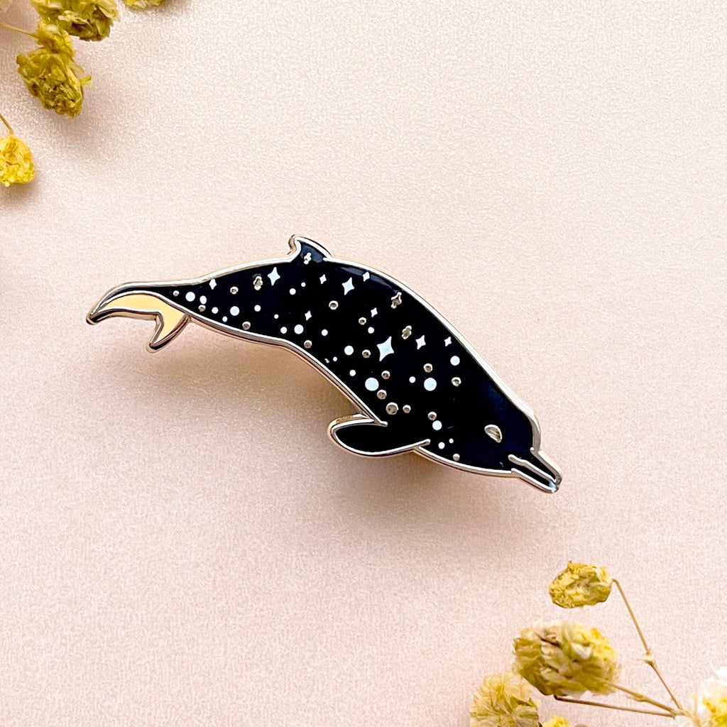 Dolphin-shaped pin with black and white pattern on a light pink background with yellow flowers.