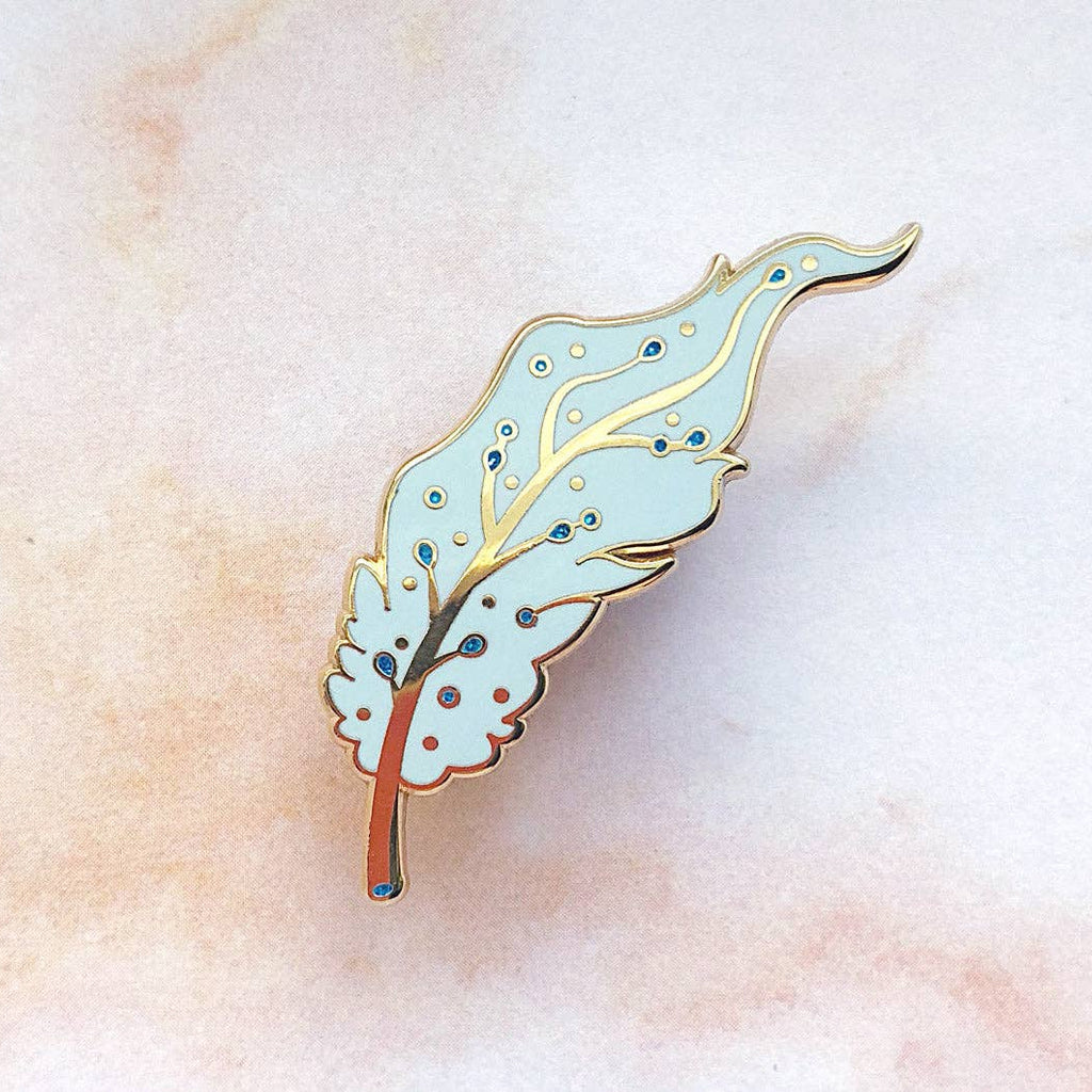 Pegasus feather enamel pin on a textured beige background
