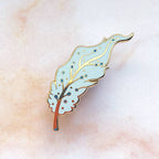 Pegasus feather enamel pin on a textured beige background