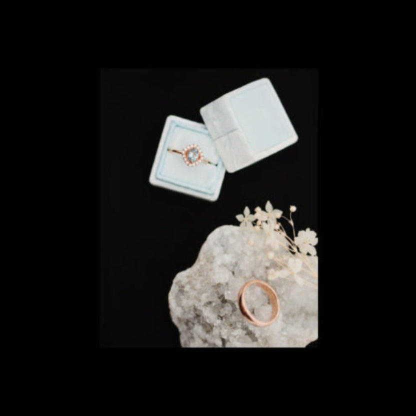Rose gold ring on a white stone with an open jewelry box in the background