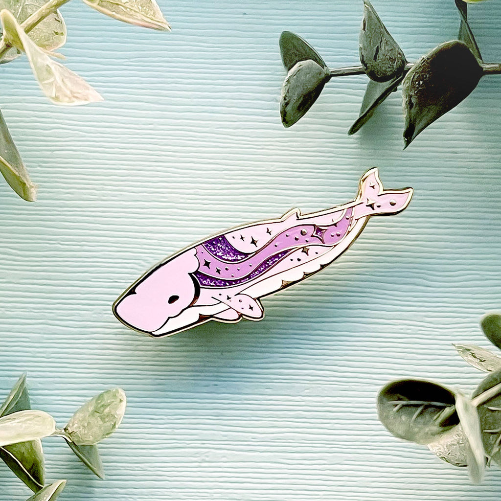 Decorative whale-shaped pin on a textured surface with green leaves