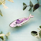 Decorative whale-shaped pin on a textured surface with green leaves