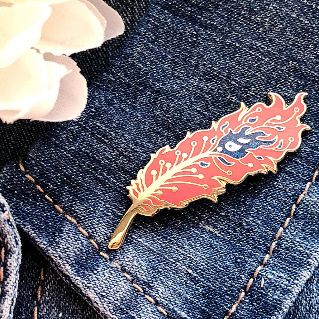 Feather-shaped pin on a denim jacket with a white flower in the background