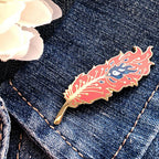 Feather-shaped pin on a denim jacket with a white flower in the background