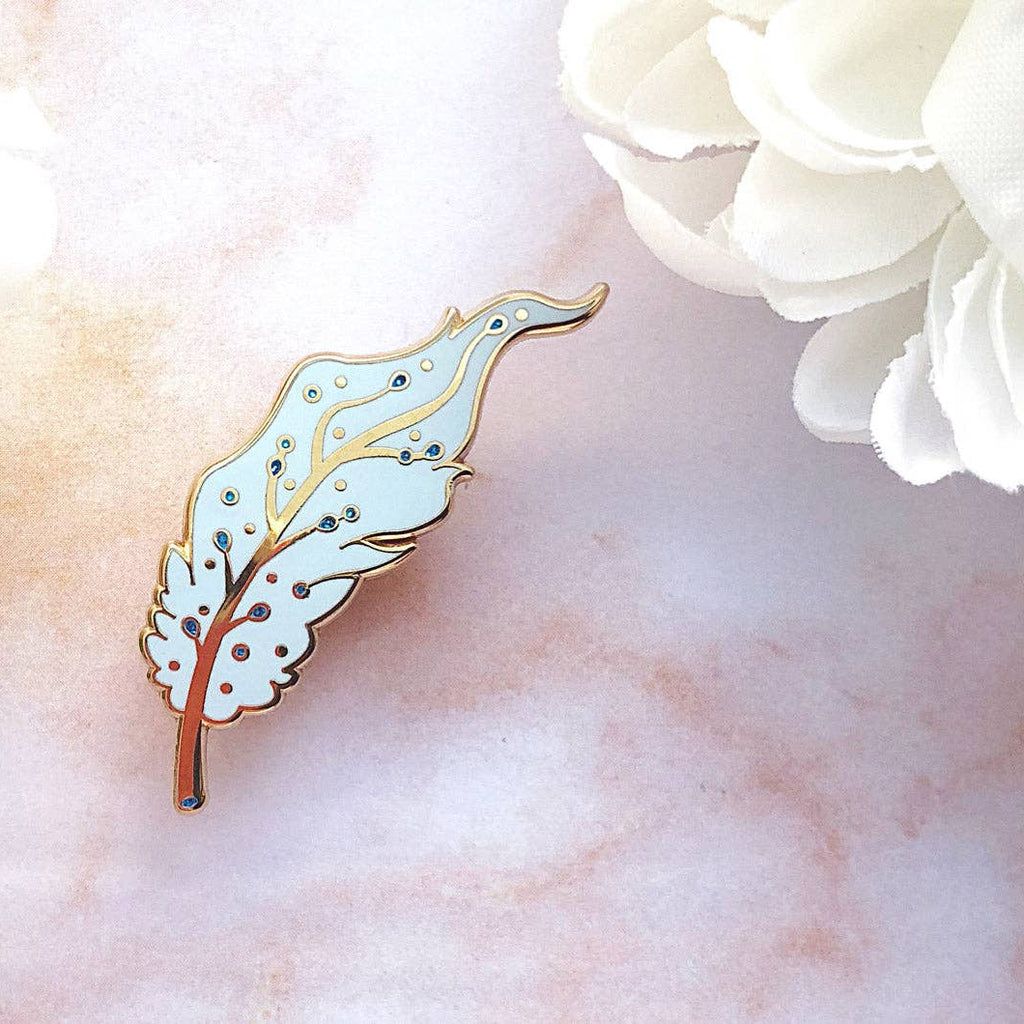 Decorative Pegasus feather pin on a marble surface with white flowers