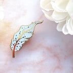 Decorative Pegasus feather pin on a marble surface with white flowers