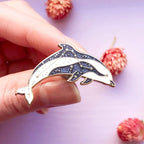 Hand holding a glittery dolphin-shaped brooch with pink dried flowers in the background