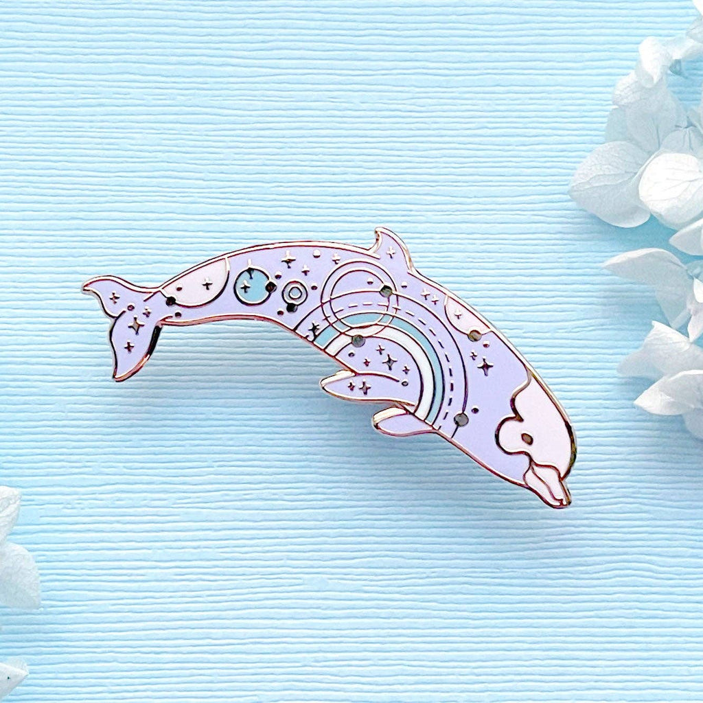 Decorative dolphin pin with intricate designs on a light blue background with white flowers.
