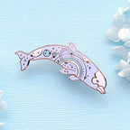 Decorative dolphin pin with intricate designs on a light blue background with white flowers.