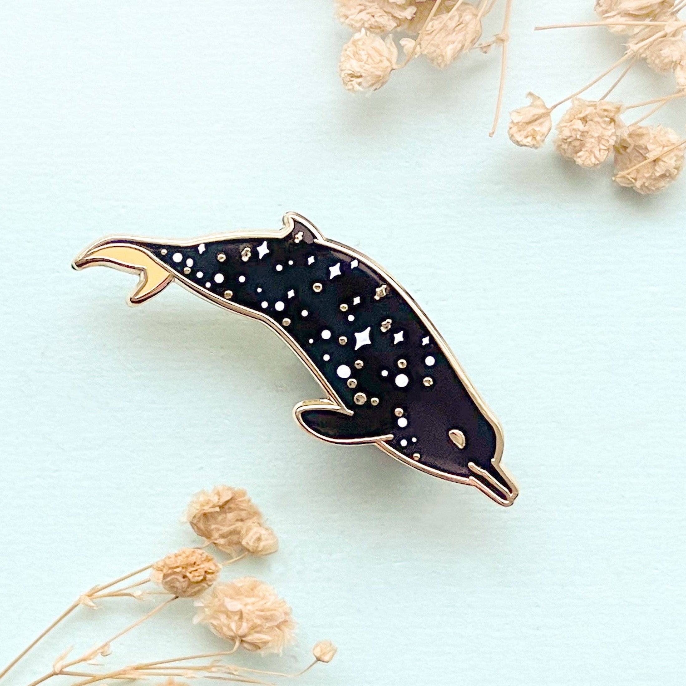 Dolphin-shaped pin with star pattern on a light blue background with dried flowers