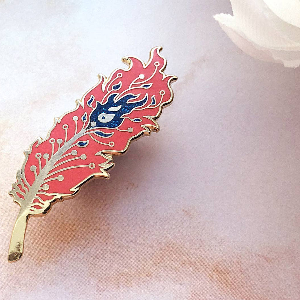 Decorative feather-shaped object with red and gold design on a soft white background