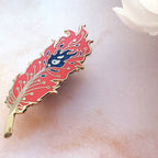 Decorative feather-shaped object with red and gold design on a soft white background