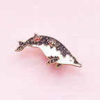 Dolphin-shaped pin with gemstones on a pink background